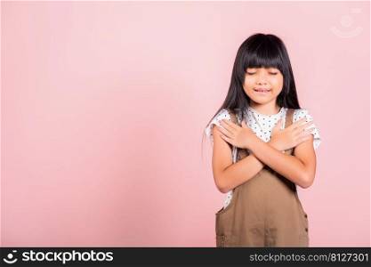 Asian little kid 10 years old doing grateful gesture and closed eyes at studio shot isolated on pink background, Happy child girl smile putting crossed palm on her chest, being thankful, Gratitude day