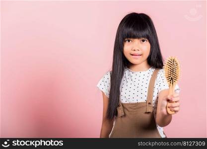 Asian little kid 10 years old hold comb brushing her unruly she touching her long black hair at studio shot isolated on pink background, Happy child girl with a hairbrush, Hair care concept