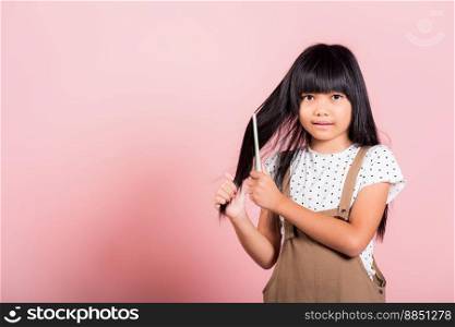 Asian little kid 10 years old hold comb brushing her unruly she touching her long black hair at studio shot isolated on pink background, Happy child girl with a hairbrush, Hair care concept