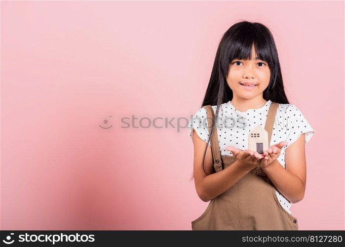 Asian little kid 10 years old hold wood house model on hands at studio shot isolated on pink background, Happy child girl with home model