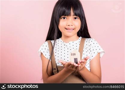 Asian little kid 10 years old hold wood house model on hands at studio shot isolated on pink background, Happy child girl with home model