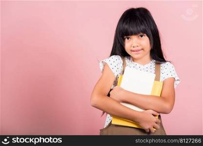Asian little kid 10 years old holding book for going to school at studio shot isolated on pink background, Happy child girl hugging textbooks dictionary, lifestyle lovely educated cheerful