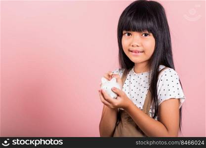 Asian little kid 10 years old holding piggy bank and looking at camera at studio shot isolated on pink background, Happy child girl lifestyle smiling with is full piggybank, Personal money savings