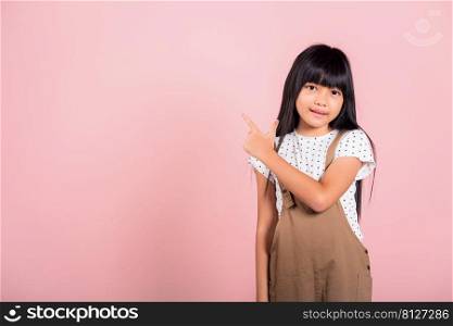 Asian little kid 10 years old point with index finger up at studio shot isolated on pink background, Happy child girl lifestyle pointing to empty place