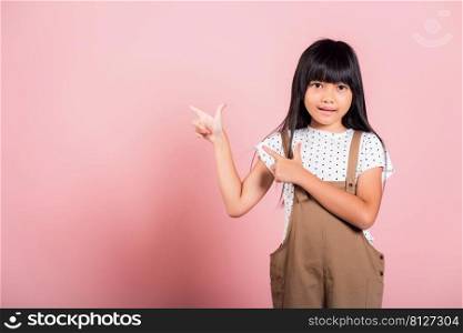 Asian little kid 10 years old point with index finger up at studio shot isolated on pink background, Happy child girl lifestyle pointing to empty place