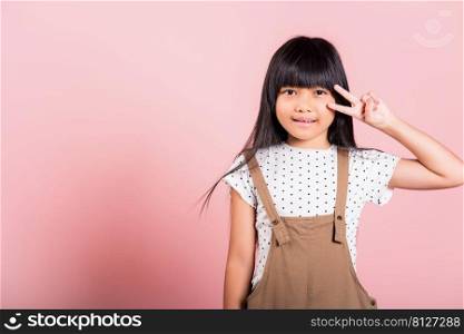 Asian little kid 10 years old show v-sign fingers gesture at studio shot isolated on pink background, Happy child girl lifestyle making victory symbol sign