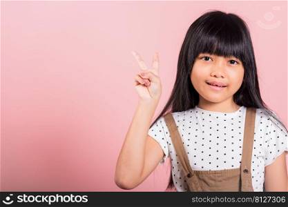 Asian little kid 10 years old show v-sign fingers gesture at studio shot isolated on pink background, Happy child girl lifestyle making victory symbol sign