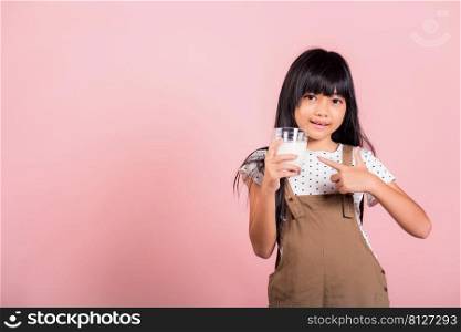 Asian little kid 10 years old smile hold milk glass drink white milk and pointing finger at studio shot isolated on pink background, Happy child girl daily life health care Medicine food