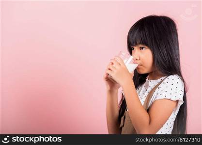 Asian little kid 10 years old smile hold milk glass drink white milk and drinking at studio shot isolated on pink background, Happy child girl daily life health care Medicine food