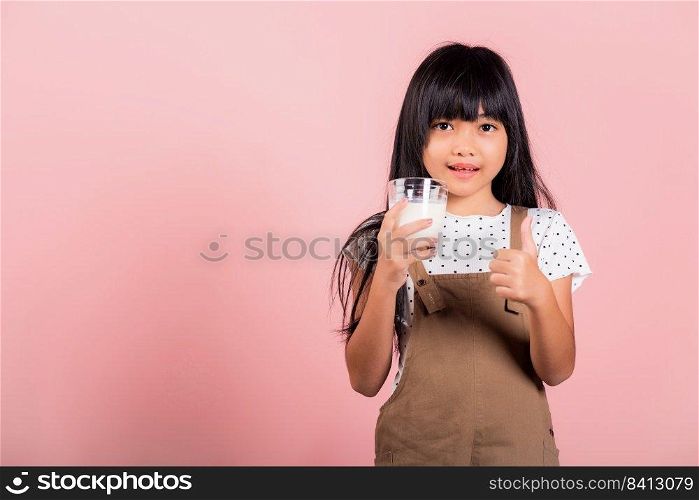 Asian little kid 10 years old smile hold milk glass drink white milk and show thumb up finger for good sign at studio shot isolated on pink background, Happy child girl daily health care medicine food