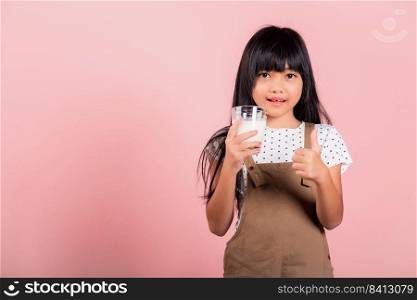 Asian little kid 10 years old smile hold milk glass drink white milk and show thumb up finger for good sign at studio shot isolated on pink background, Happy child girl daily health care medicine food