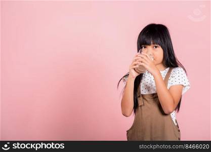 Asian little kid 10 years old smile hold milk glass drink white milk and drinking at studio shot isolated on pink background, Happy child girl daily life health care Medicine food