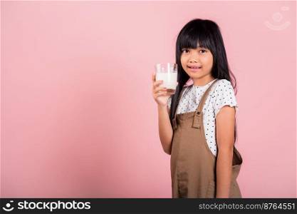 Asian little kid 10 years old smile hold milk glass drink white milk at studio shot isolated on pink background, Happy child girl daily life health care Medicine food