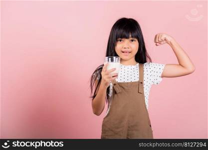 Asian little kid 10 years old smile holding milk glass and show power strong gesture at studio shot isolated on pink background, Portrait of Happy child girl daily life health care medicine food