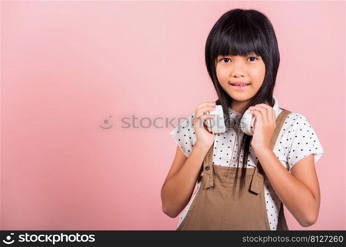 Asian little kid 10 years old smiling listening music wearing wireless headset around neck at studio shot isolated on pink background, Happy child girl lifestyle listen music with headphones