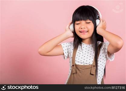 Asian little kid 10 years old smiling listening music wearing wireless headset at studio shot isolated on pink background, Happy child girl lifestyle listen music with headphones keeping eyes closed
