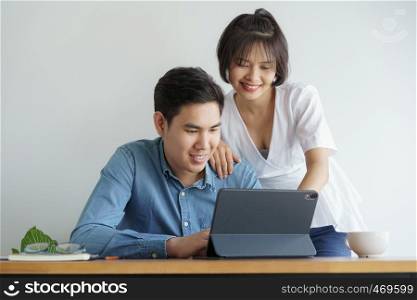 Asian love couple sit chair in the living room and working on tablet they is smiling happily.