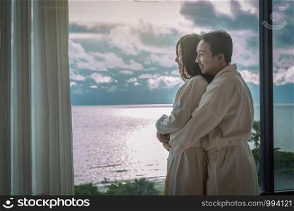 Asian lovers in bathrobe suit hugging and sightseeing the sea beach when waking up from the bed in luxury hotel in morning, Life style and holiday with couple concept