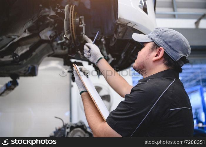Asian male car technician car maintenance for customers according to specified vehicle maintenance checklist. Disk brake pad wear automotive repairing on vehicle. Safety inspection check service