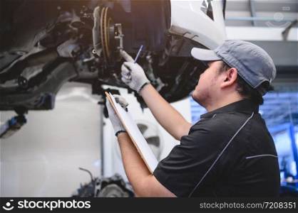 Asian male car technician car maintenance for customers according to specified vehicle maintenance checklist. Disk brake pad wear automotive repairing on vehicle. Safety inspection check service