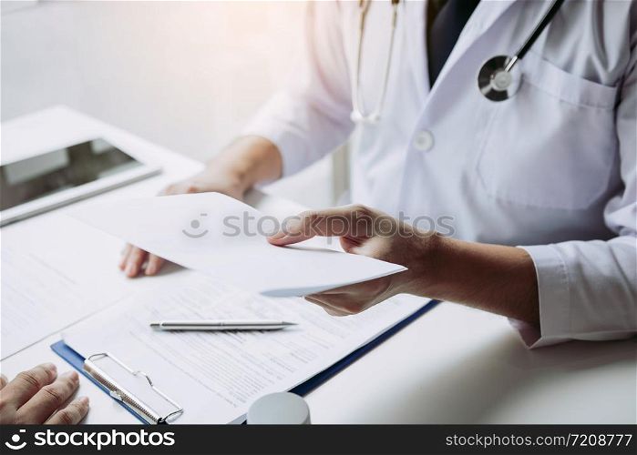 Asian male doctor talking in clinic room and handing a prescription to the patient.