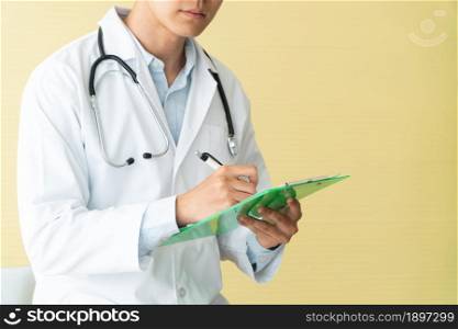 Asian male doctor writing health report, Medical care, or prescription on the green clipboard in hospital. Concept of Medical and healthcare.