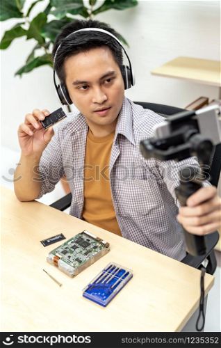 asian male IT vlogger and blogger live Technology upgrand on laptop memory ram using mobile phone recording live vlog video. Online influcencer on social media concept.