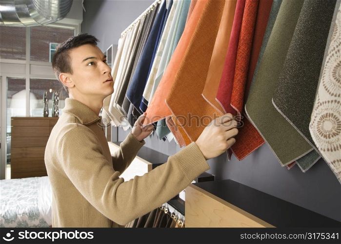 Asian male looking at fabric swatches in retail store.