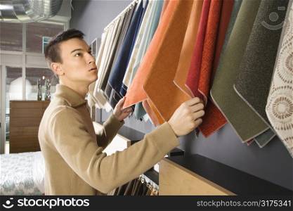 Asian male looking at fabric swatches in retail store.