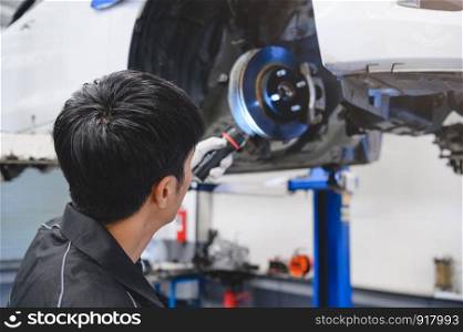 Asian male mechanical hold and shining flashlight to examine car disk brake pad wear of automotive vehicle. Safety suspension inspection check service maintenance for customer before road trip concept