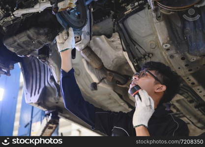 Asian male mechanical hold and shining flashlight to examine car under chassis of automotive vehicle. Safety suspension inspection check service maintenance for customer before road trip concept