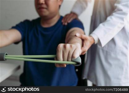 Asian male physical therapist descent working with patient doing stretching exercise with a flexible exercise band in clinic room.