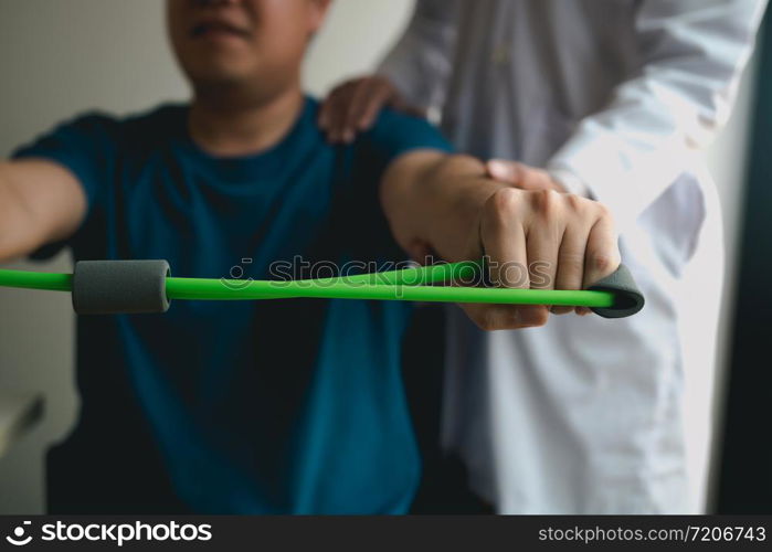 Asian male physical therapist descent working with patient doing stretching exercise with a flexible exercise band in clinic room.