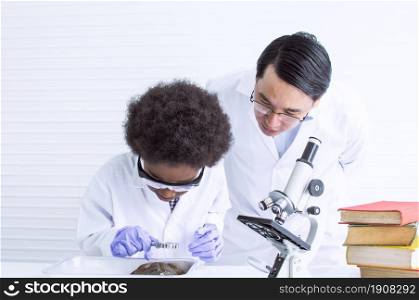 Asian male teacher is teaching science and experiment for a frog to African black boy in classroom at school. Education Concept.