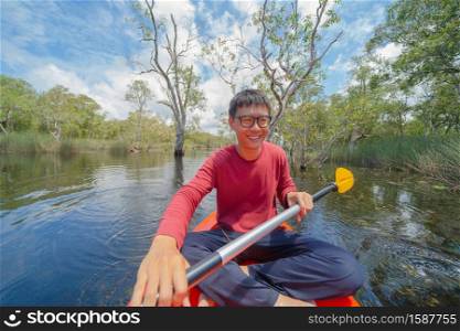 Asian man, a tourist, paddling a boat, canoe or kayak with trees in Rayong Botanical Garden, Paper Bark Tropical Forest in national park in Thailand. People lifestyle adventure activity recreation.