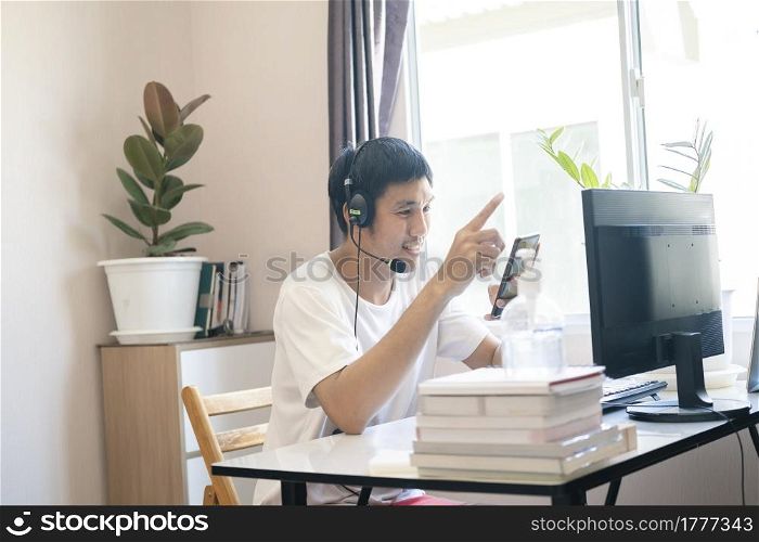 Asian man administrator staff call center in home service office assistance work from home looking data customer from computer communication during coronavirus covid-19