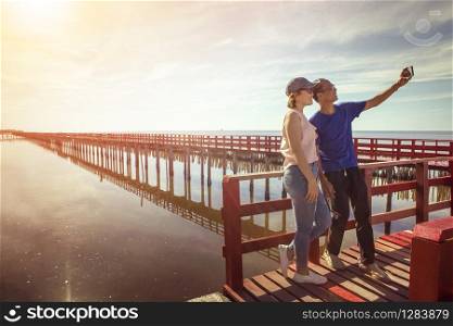asian man and woman taking a photo on red wood bridge against sun rising sky