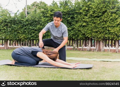 Asian man and woman training yoga outdoors in meditate pose sitting on green grass. Young couple practicing doing stretching in nature a field garden park together. Meditation health care concept