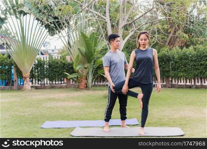 Asian man and woman training yoga outdoors in meditate pose stand on green grass. Young couple practicing doing stretching in nature a field garden park together. Meditation health care concept
