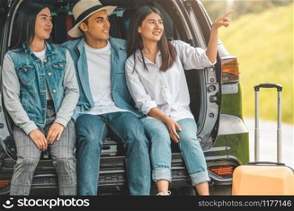 Asian man and women relaxing in back of car trunk during travel in summer. Transportation and people lifestyles concept. Group of happy friendship sit and looking nature view. Relaxation in vacation