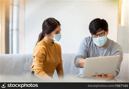 Asian Man Architect present his idea to woman client. Male Interior Designer work on laptop with partner in meeting. People in protective face masks for prevent pandemic virus during talking business