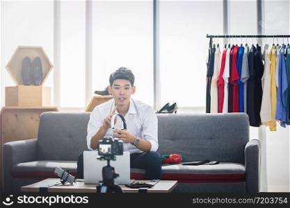 Asian man blogger broadcasting a video for selling product online such as Hats, shoes, headphones, clothing, safety headers.Shopping online concept at home