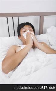 Asian man blowing nose in bed