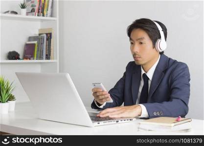 Asian Man Call Center in Suit Wear Headset Answer Customer Questions by Smartphone and Laptop. Asian man call center working in Office