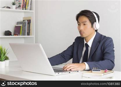 Asian Man Call Center in Suit Wear Headset or Headphone Contacting and Service the Customer Via Internet in Office. Asian man call center working with laptop
