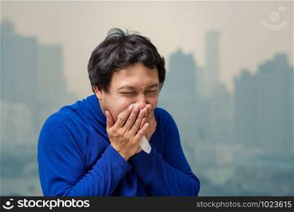 Asian man coughing with Tissue against air pollution with at the balcony of High Apartment which can see pollution and heavy fog over the bangkok cityscape background, healthcare concept