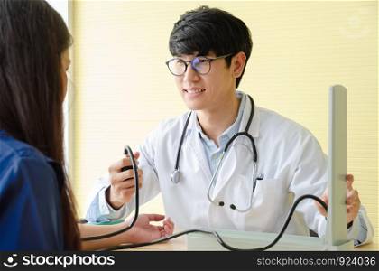Asian man doctor taking blood pressure of female patient with clinical mercury manometer at office. Healthcare and medical check up concept
