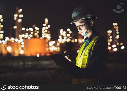 Asian man engineer using digital tablet working late night shift at petroleum oil refinery in industrial estate. Chemical engineering, fuel and power generation, petrochemical factory industry concept