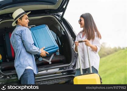 Asian man helping woman to lifting suitcase from car during travel in long weekend. Couple have road trip in vacation with yellow luggage. People lifestyle and transportation concept. Nice guy theme