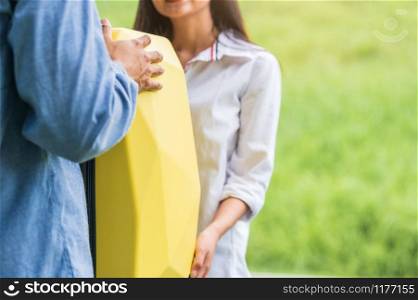 Asian man helping woman to lifting suitcase from car during travel in long weekend. Couple have road trip in vacation with yellow luggage. People lifestyle and transportation concept. Nice guy theme